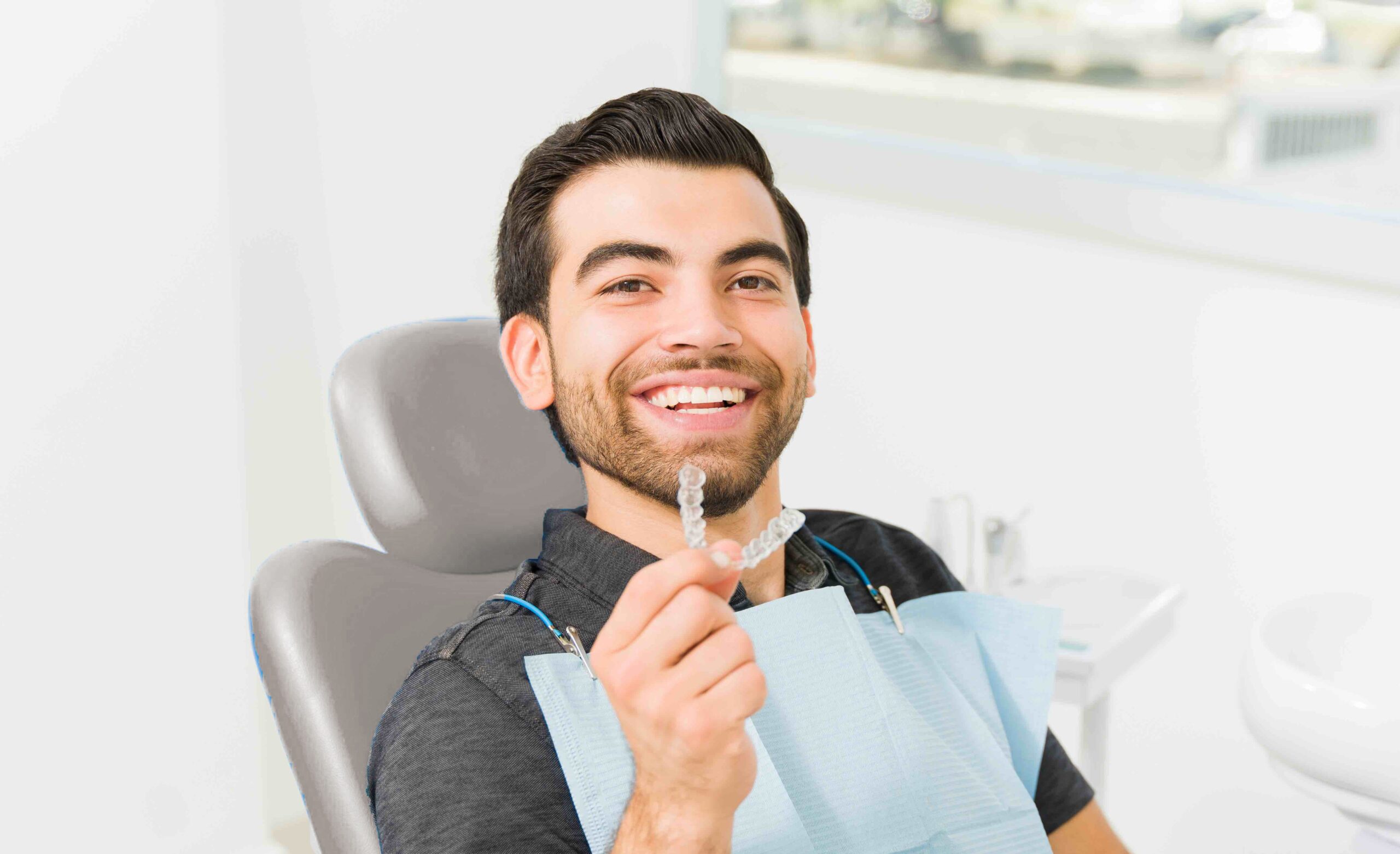 Man smiling and holding his Invisalign® aligner while wearing a dental bib