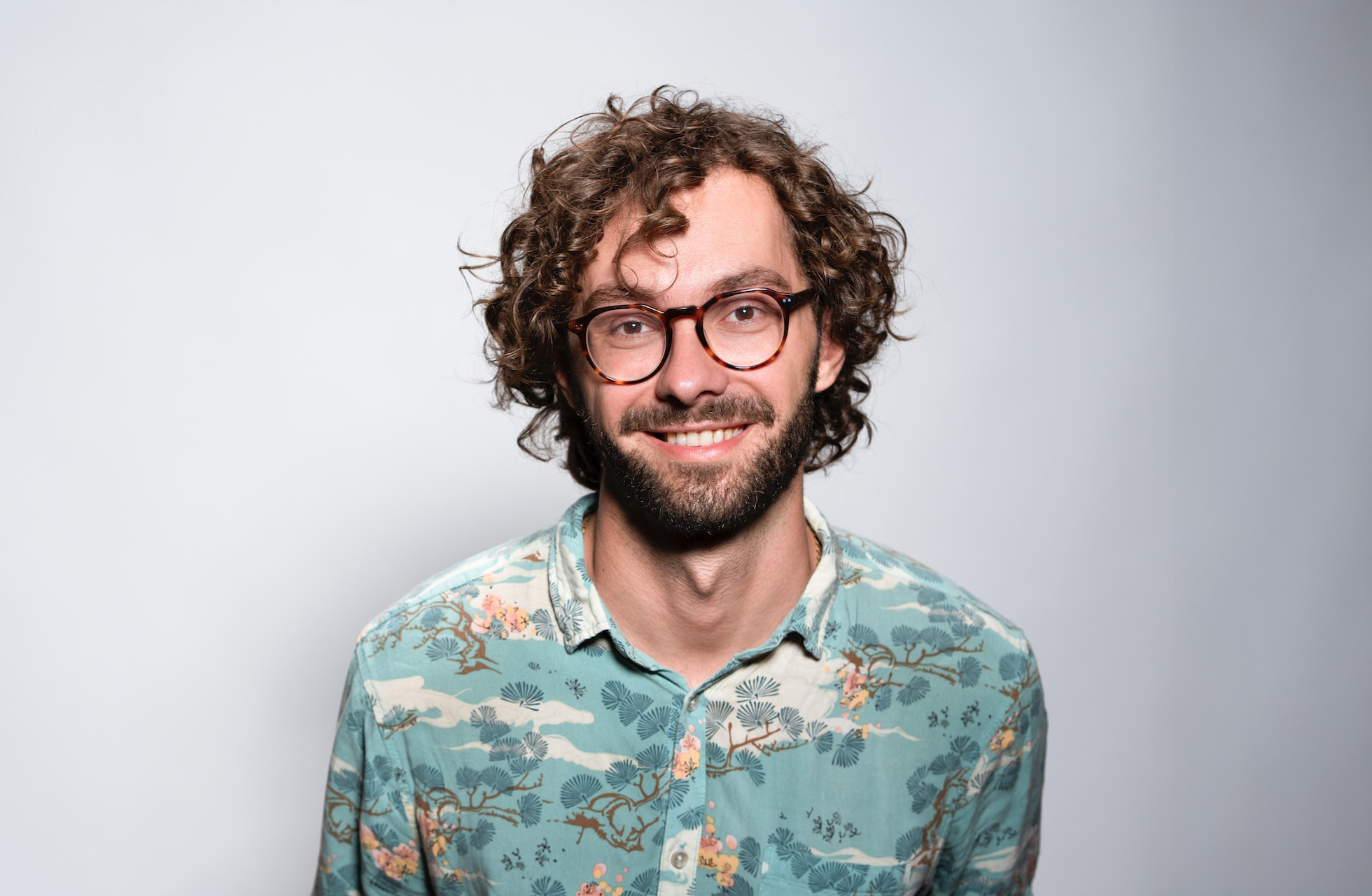 A cheerful man with curly hair and glasses, showcasing a bright smile.