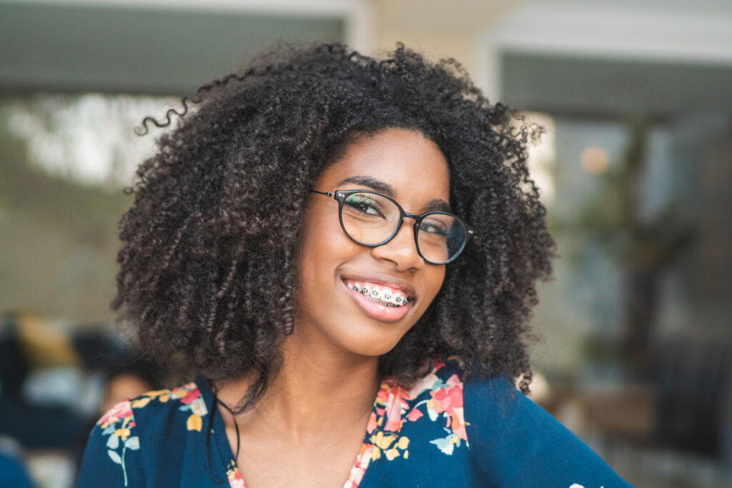 Beautiful woman smiling with traditional metal braces, glasses, and vibrant curls