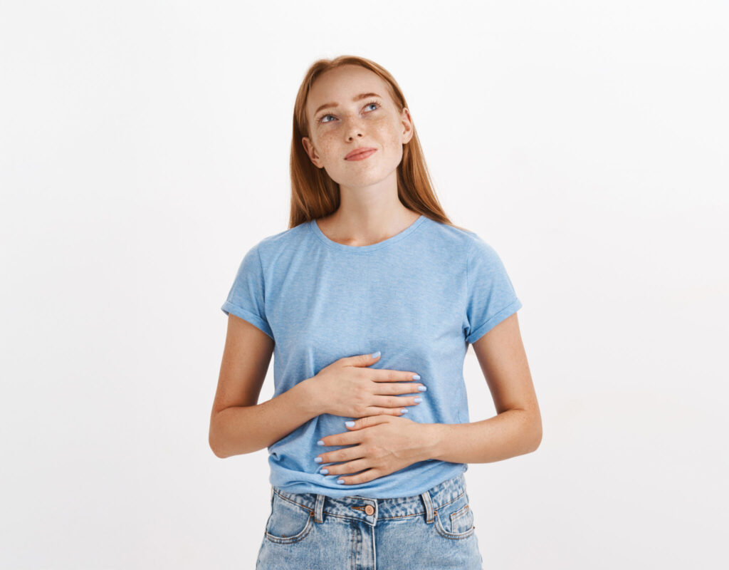Teen with vibrant red hair with her hands on her stomach and looking up inquisitively