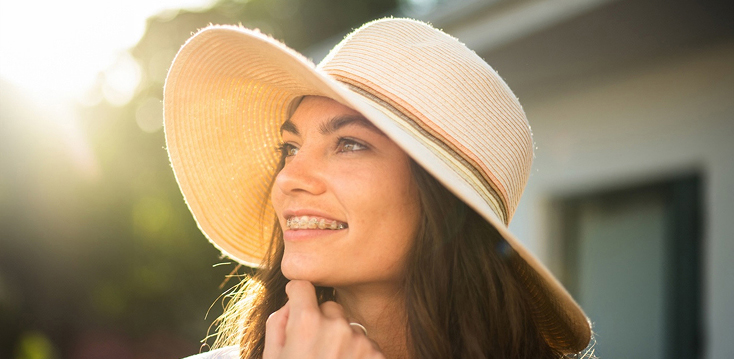 smiling woman in hat wearing braces outdoors in the evening
