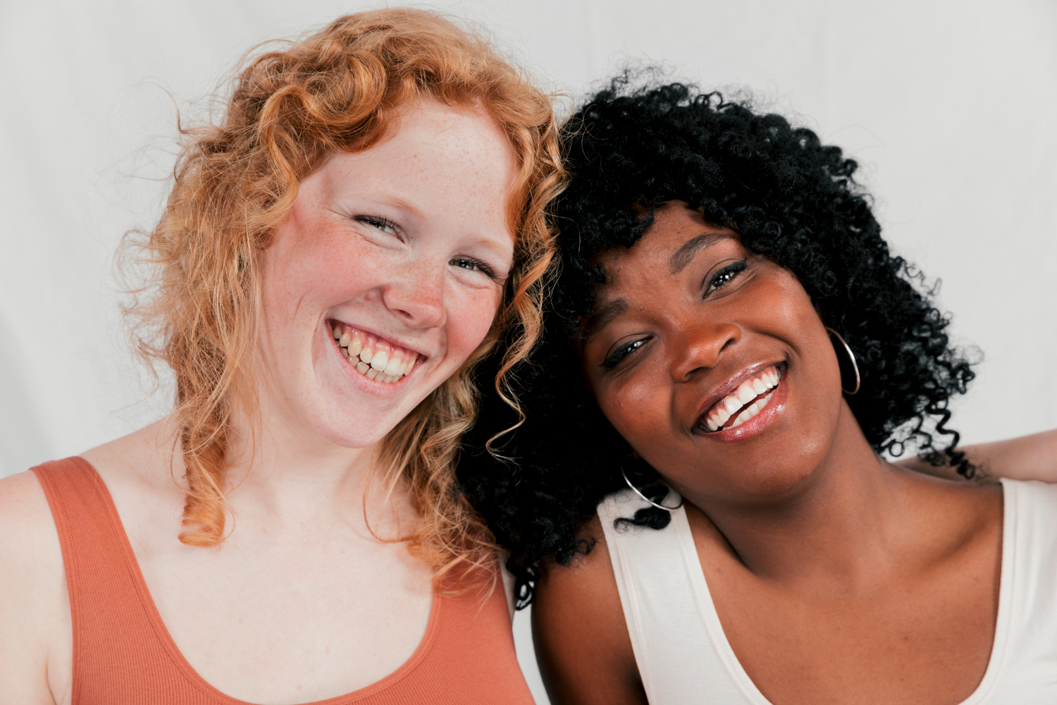 Two friends with aesthetic smiles leaning into one another and smiling
