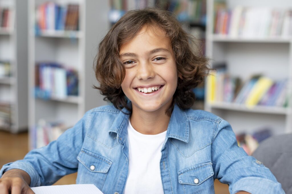 A boy sitting in a library smiling.