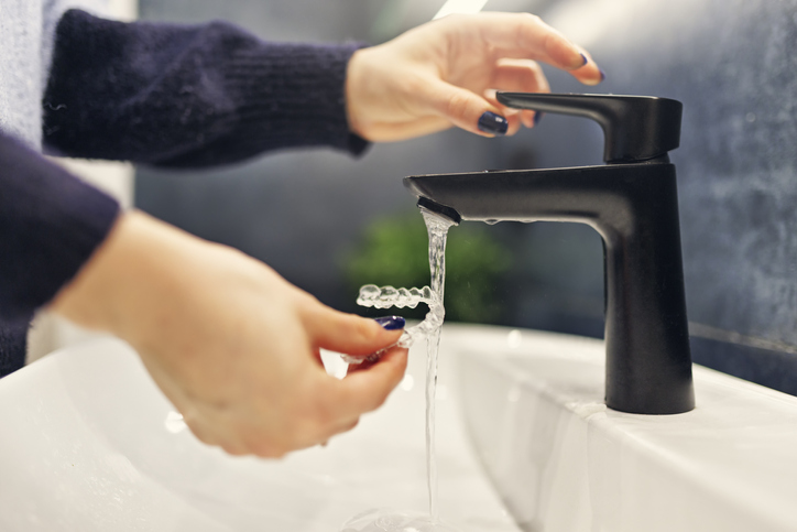 Woman with midnight blue nails rinsing her clear plastic retainer in the sink