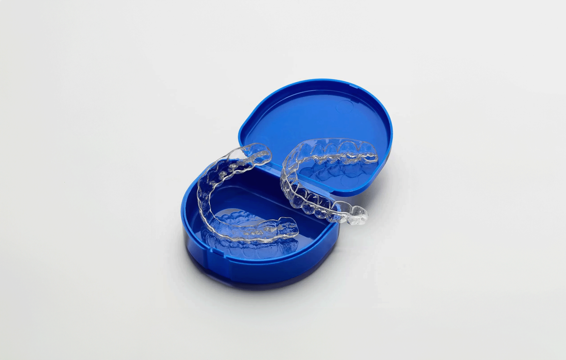 Essix clear retainers in a blue case, on a white table.