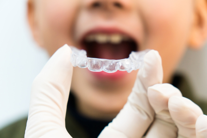 A doctor holding clear aligners up to a little boy's mouth